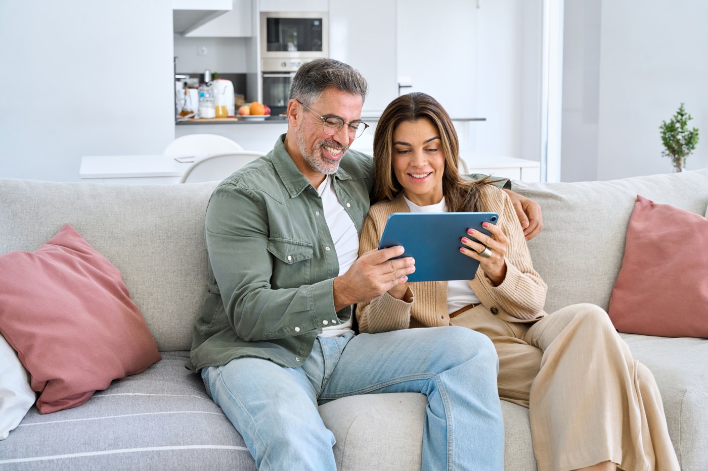 Casal sentado no sofá de casa, sorrindo, lendo e assinando no tablet