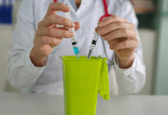 Profissional descartando seringas em um recipiente para perfurocortantes