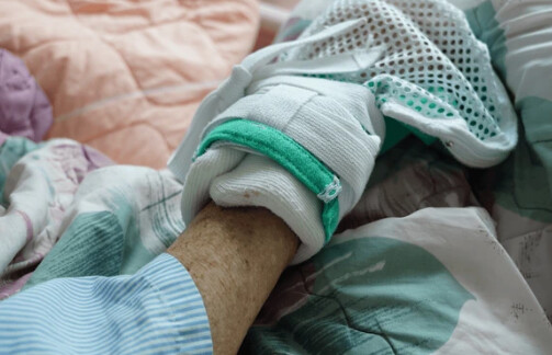 Mão de um paciente acamado, protegida, sobre a roupa de cama