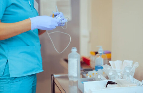 Profissional de enfermagem com luvas preparando um equipo de infusão na bancada de materiais
