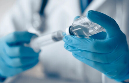 Profissional com luvas azuis preparando um medicamento com seringa e frasco