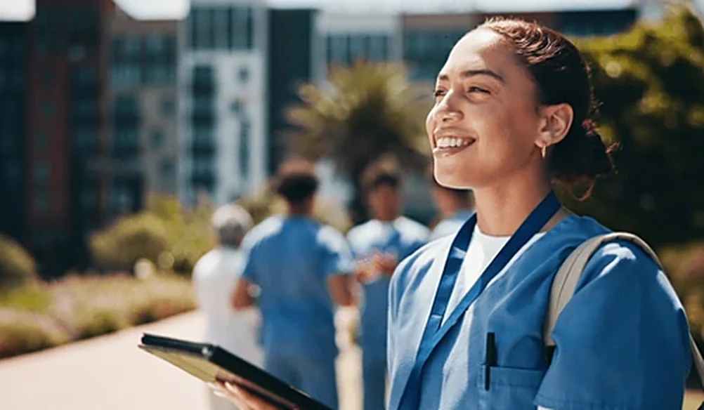 Profissional de saúde sorridente, de uniforme azul, segurando um tablet