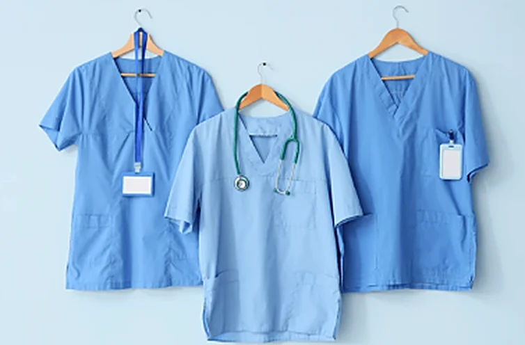 Três uniformes azuis de profissionais de saúde pendurados em cabides
