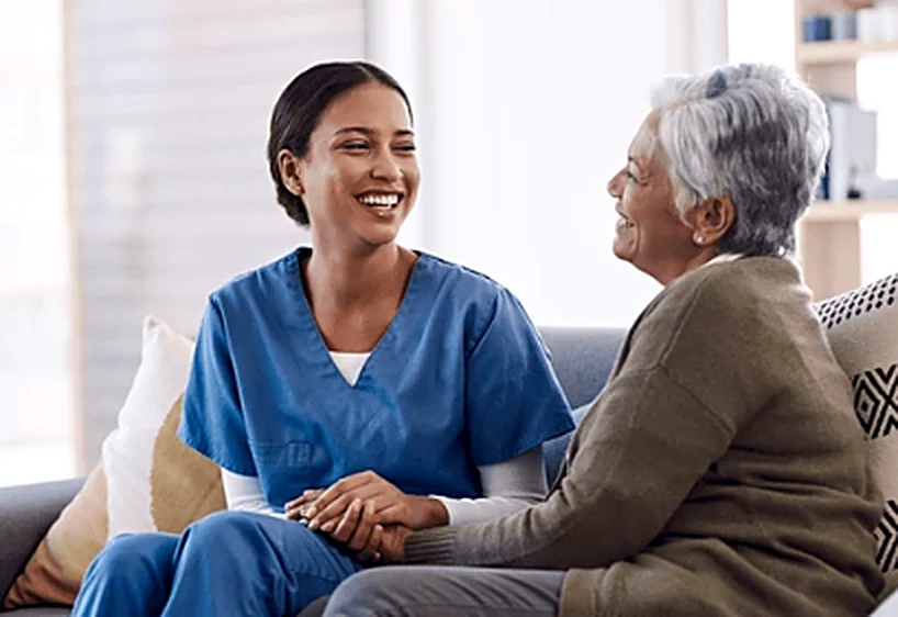 Cuidadora sorridente conversando com uma senhora idosa no sofá