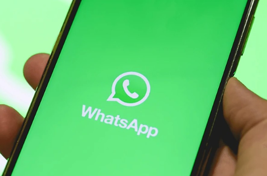 Mão segurando o celular com o WhatsApp aberto na tela