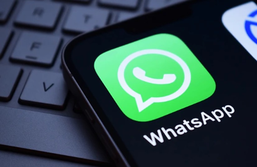 Celular sobre o teclado do computador com o ícone do WhatsApp em destaque na tela